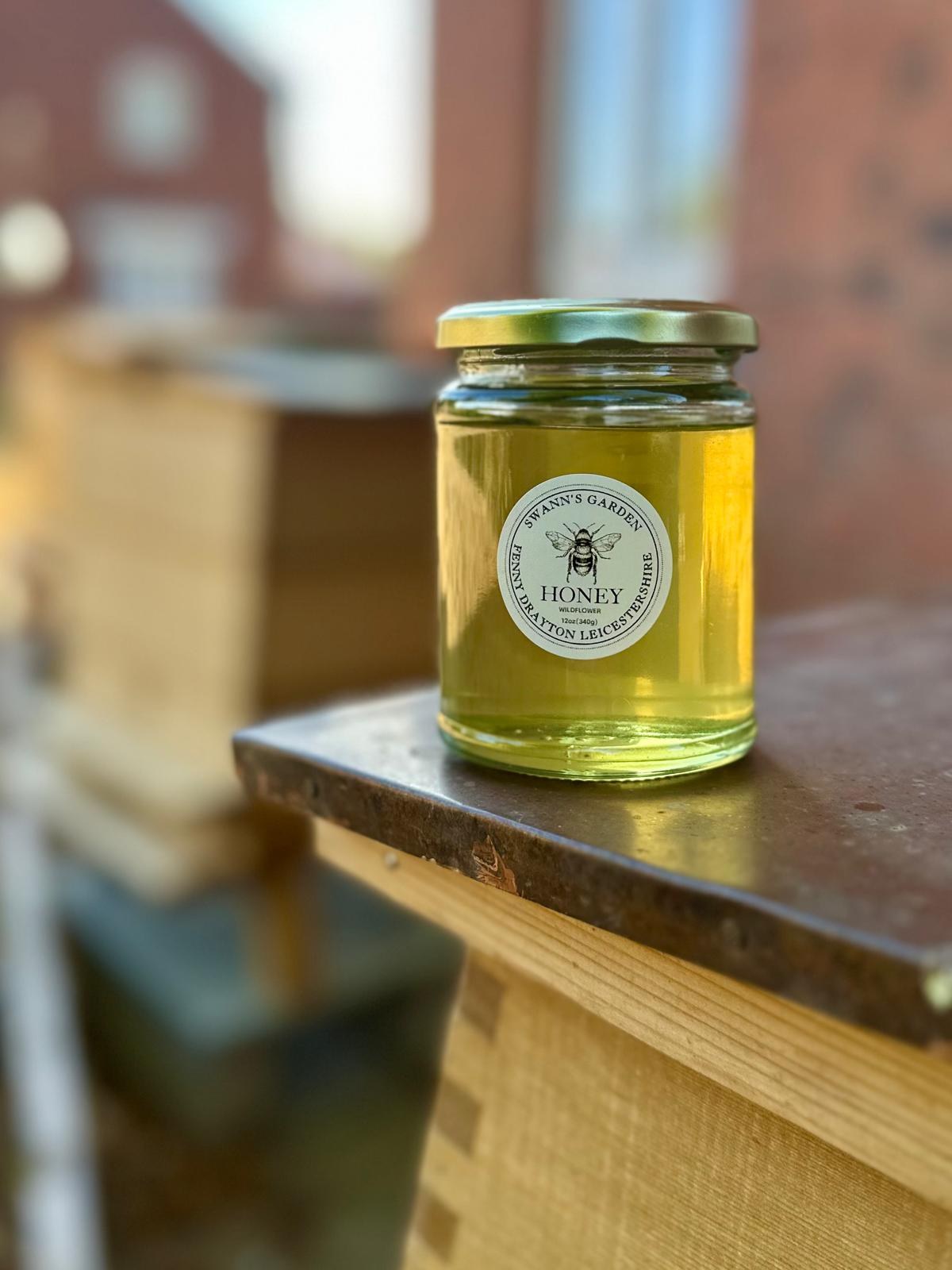 Jar of Swann's Garden wildflower honey beside a hive
